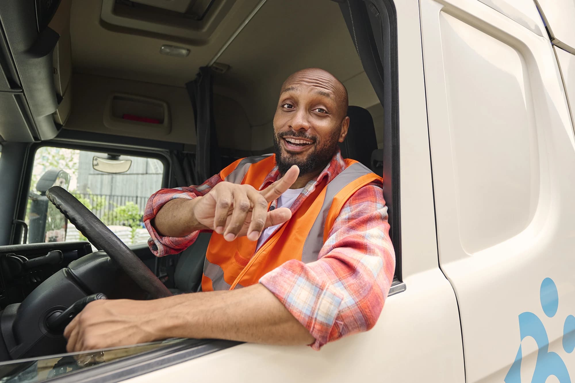 Chauffeur poids lourd en gilet fluorescent sourit et pointe depuis la cabine — emplois de transport via Accent
