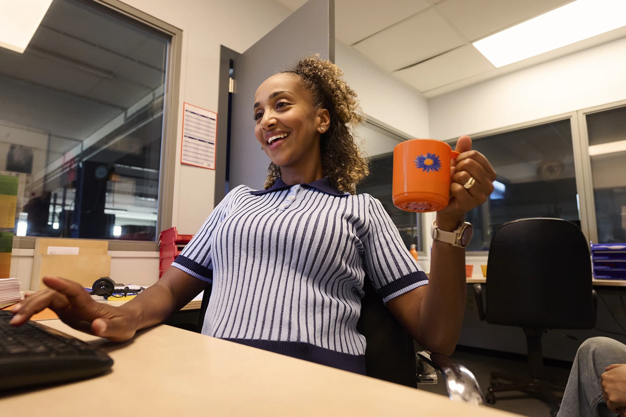 Employé administratif sourit avec une tasse de café derrière son ordinateur — emplois de bureau avec plaisir au travail via Accent